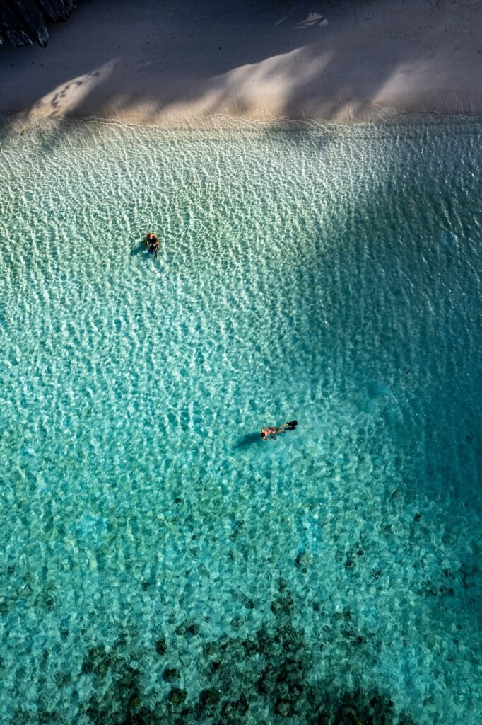 Aerial view of two snorkellers in shallow turquoise water at Banuang Daan, Coron, Palawan, Philippines