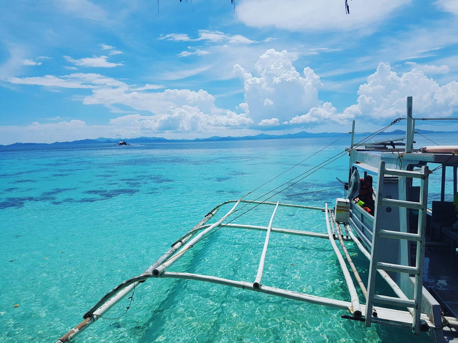 A white and blue outrigger boat on calm water in Coron Bay, Palawan, used for wreck-diving day trips