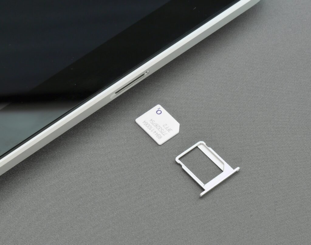 A SIM card and an empty SIM tray on a light surface beside the edge of a smartphone